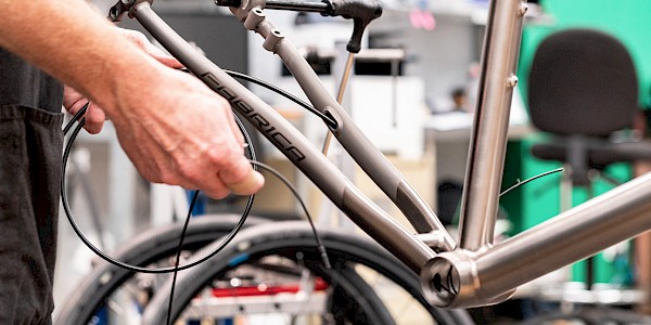 Bicycle mechanic feeding a disc brake hose through a titanium bicycle frame