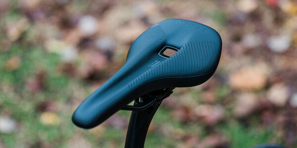 An Ergon saddle fitted to a bicycle with a carbon seat post, shot against a leafy background