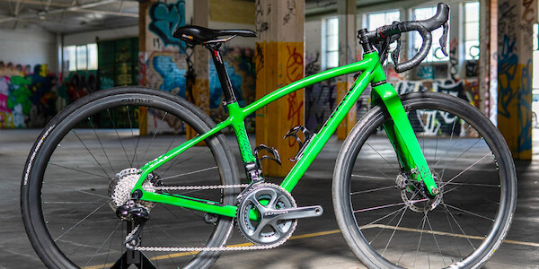 A custom-designed carbon Plane Frameworks bicycle in bright green, shot inside a graffiti-covered car park
