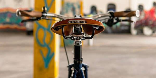 A Brooks B17 saddle in Honey, viewed from behind on a Blueberry Muffintop Surly Straggler bike