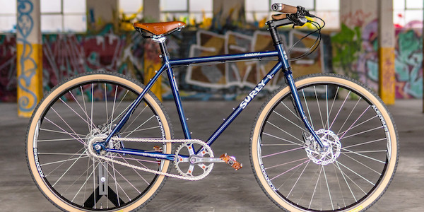 A custom-built Surly Straggler bike in Blueberry Muffintop, freestanding inside a heavily graffitied car park