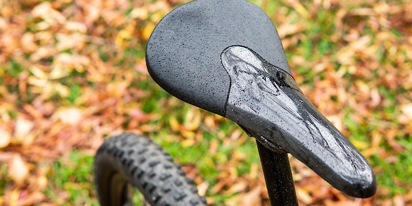 A Tune carbon Komm Vor Plus saddle on a Ibis Mojo 3 carbon mountain bike, autumn leaves on the ground in the background