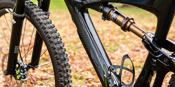 Rear shock and frame detail on a Ibis Mojo 3 carbon mountain bike, against a leafy park background