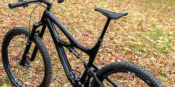 A custom-built Ibis Mojo 3 carbon mountain bike in a leafy park, elevated viewed from the left side