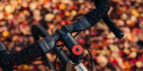 A red Garbaruk top cap fitted to a titanium road bike, shot from above against an autumnal leaf backdrop