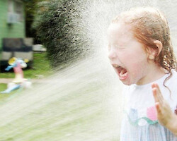 A little redheaded girl getting sprayed in the face by a hose. She's not enjoying it.