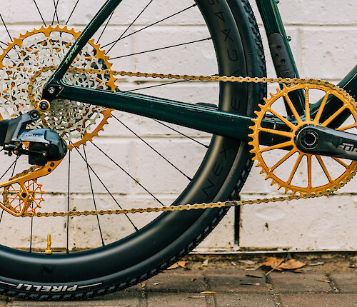 Gold Garbaruk drivetrain/gear components fitted to a Time carbon bicycle. A white brick wall is in the background.