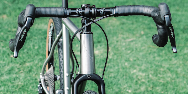 Headtube and handlebar detail on a custom-built Bossi Grit SX titanium gravel bike, on a green lawn