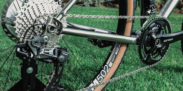 Drivetrain detail on a custom-built Bossi Grit SX titanium bicycle, standing on a lush lawn