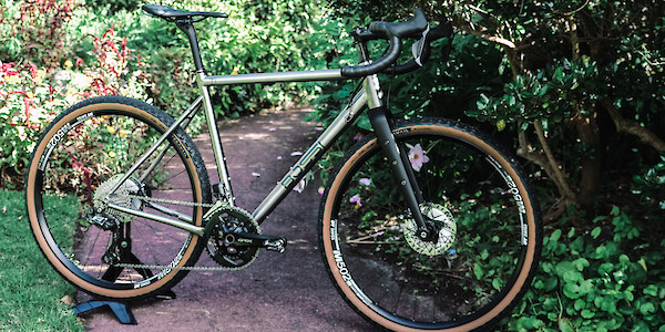 A custom-built Bossi Grit SX titanium on a paved garden path, surrounded by foliage