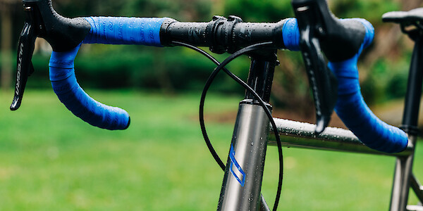 Handlebar and headtube detail on a Bossi Summit titanium road bike, showing the hand-painted head tube decal and matching blue handlebar tape