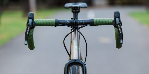 Front view of a Bossi Grit SX titanium bike, showing the custom-painted head tube decal and green handlebar tape, on a city park pathway