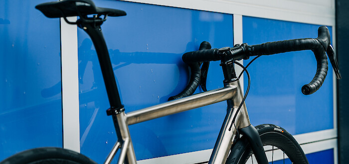 A custom-built Bossi Strada titanium road bike, leaning against blue and silver panelling