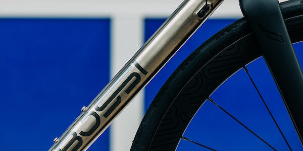Downtube logo detail on a titanium Bossi Strada road bike, segmented blue panels in the background