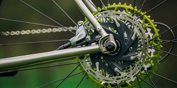 Disc brake detail on a Bossi Grit SX titanium gravel bike, showing the rotor, with a green Garbaruk cassette in the background