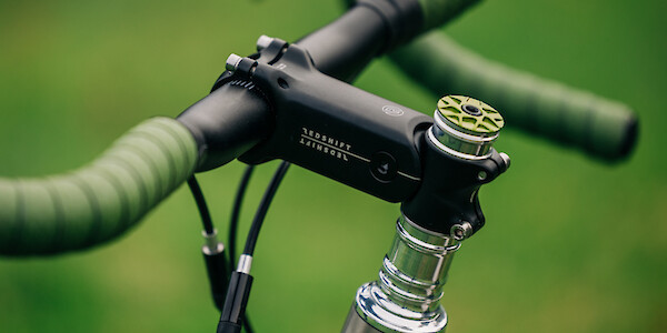 Details of a green Garbaruk top cap, Redshift Shockstop headstem and Ciclovation Advanced Grind bar tape on a Bossi Grit SX titanium gravel bike