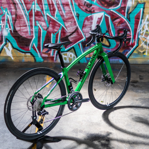 A custom-made Plane Frameworks carbon bicycle, standing in front of a graffiti-covered wall