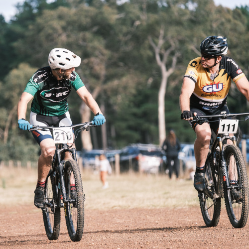 Two mountain bikers, one in a Bio-Mechanics Cycles & Repairs jersey, chatting during a race