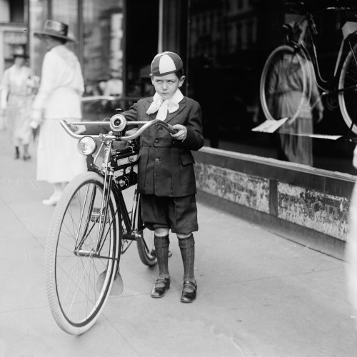 An old black and white photo showing a young boy with a bicycle, looking distrustful