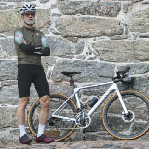 A mature bearded gentleman posing against a wall with his road bicycle