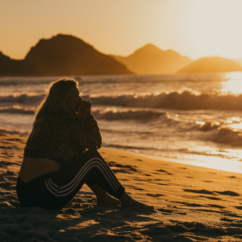 A woman sitting on the beach in the sunset, anxiously looking at the waves