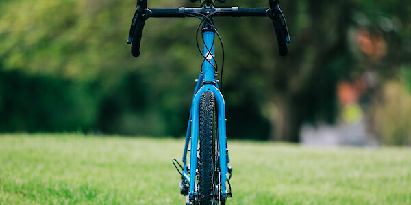 A blue Genesis Croix de Fer 40 gravel bike, viewed from the front, against a backdrop of greenery