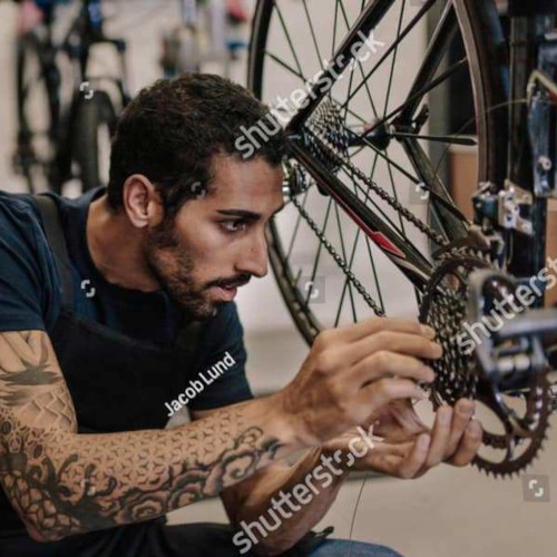 A male model posing as a bicycle mechanic. He is holding a critical gear component on entirely the wrong area of the bike. It is, to actual mechanics, hilarious.
