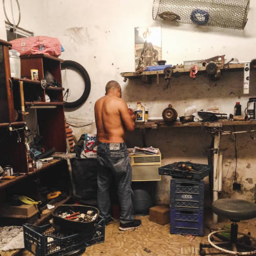A shirtless man works in a crowded, untidy workshop. His back is to us. There's stuff everywhere. This is my nightmare.