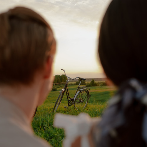 A man and woman gazing at a bicycle in a field. The picture is taken from close behind and between their heads. It's less exciting than it sounds.