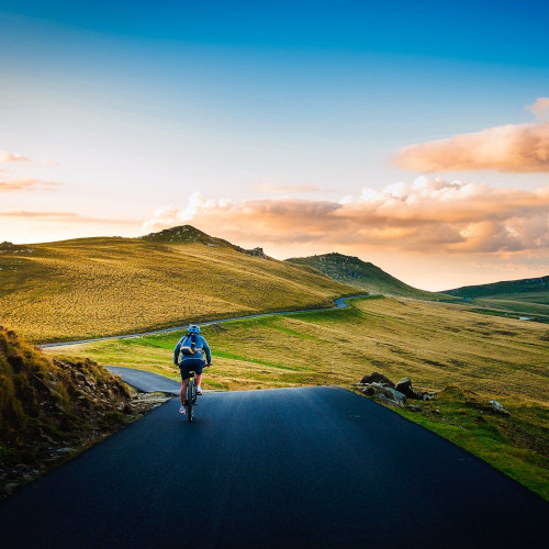 A bike rider cycling away on a very smooth road, heading into an idyllic hills landscape.