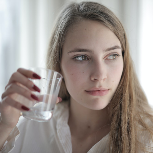 A woman pausing in the act of drinking a glass of water, as if she's just remembered something