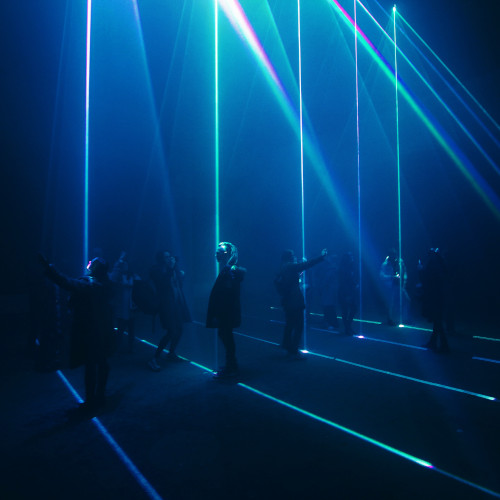 People standing in a dark room which is lit with lasers. Some are pointing in different directions.