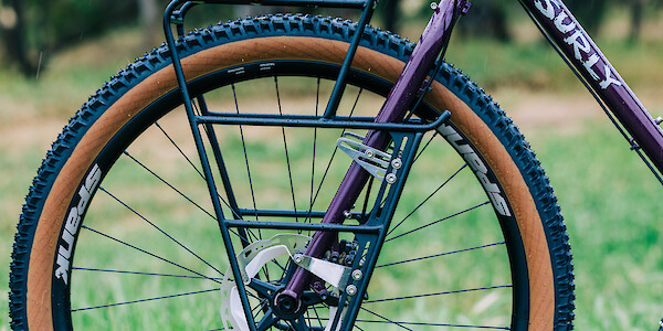 A black Surly Nice front rack on a custom-built Surly Karate Monkey bicycle in Eggplant, shot from the side in a green field.