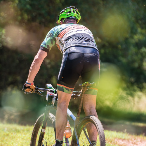 Rear view of a mountain biker out on the trails, standing up on the pedals of his bike, wearing cycling kit.