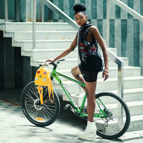A young woman wearing high fashion (including platform shoes), posing on a bicycle, next to a staircase.