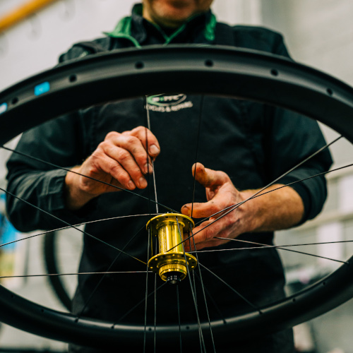 A professional bicycle mechanic at Bio-Mechanics Cycles & Repairs, lacing up a carbon bicycle wheel with a gold hub