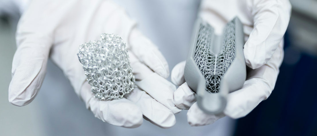 A person holding two lumps of material in their gloved hands, one metal, one three-D printed