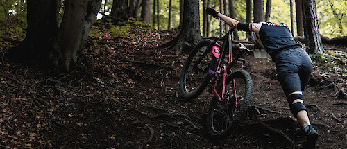 A mountain biker pushing their bike up a forest slope, head down.