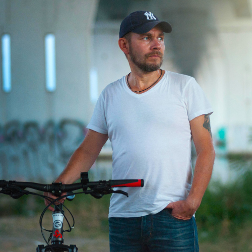 A man in a graffitied park, holding a mountain bike, and looking off into the distance