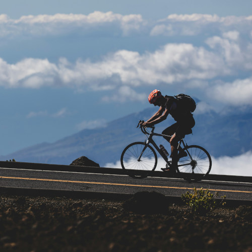 A cyclist rides up a steep hill on a road bike, mountains in the background