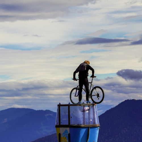 A man standing on a structure, looking down at the mountain bike he's holding