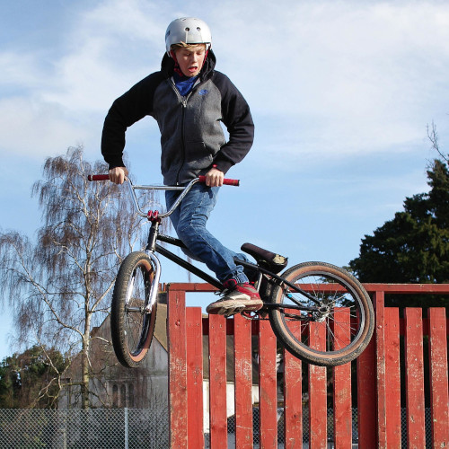 A young man jumping a BMX, looking down at the ground with an expression of horror.