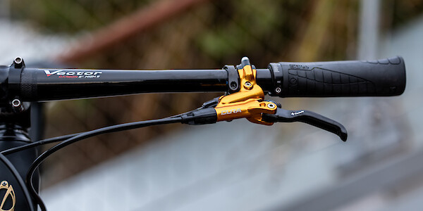 SQLab 70X handlebar grip fitted to a set of Syntace handlebars, next to a gold Formula brake. A chain link fence is out of focus in the distance.