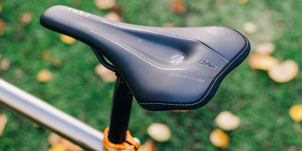 SQLab 611 saddle, fitted to a titanium Bossi gravel bike, photographed from above against a leaf-strewn lawn background.