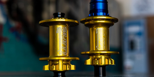 A pair of gold Tune bicycle hubs on a reflective concrete surface