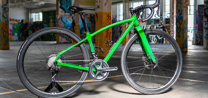A bright green carbon Plane Frameworks custom-made bicycle inside a graffiti-covered car park