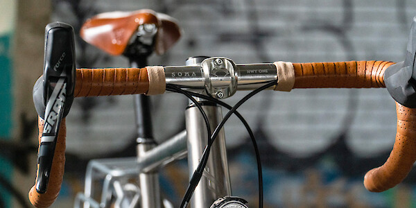Handlebar detail on a Bossi Grit titanium commuter bike, with Brooks leather bar tape and matching saddle in Honey, viewed from the front right