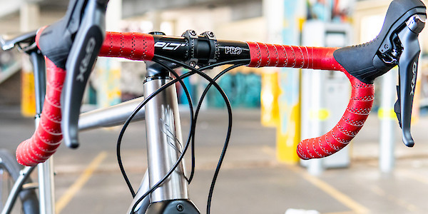 A titanium Bossi Grit gravel bike with red handlebar tape, viewed up close from the front right side