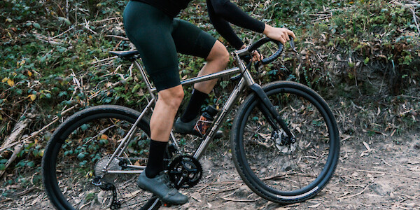 Cyclist riding a Bossi Grit SX titanium gravel bike up an off-road trail