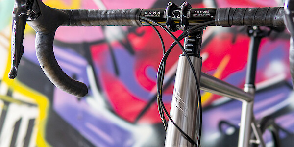 Head tube and handlebar detail on a Bossi titanium bike, a colourful graffiti wall in the background
